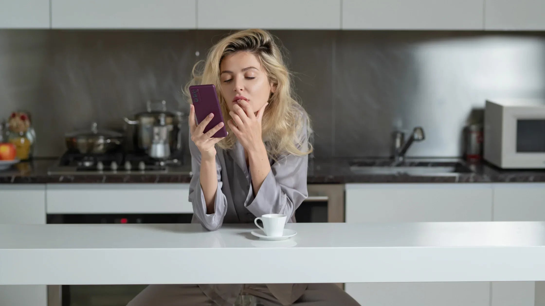 girl on her phone putting her lip with a cup of coffee in the kitchen numen wellness